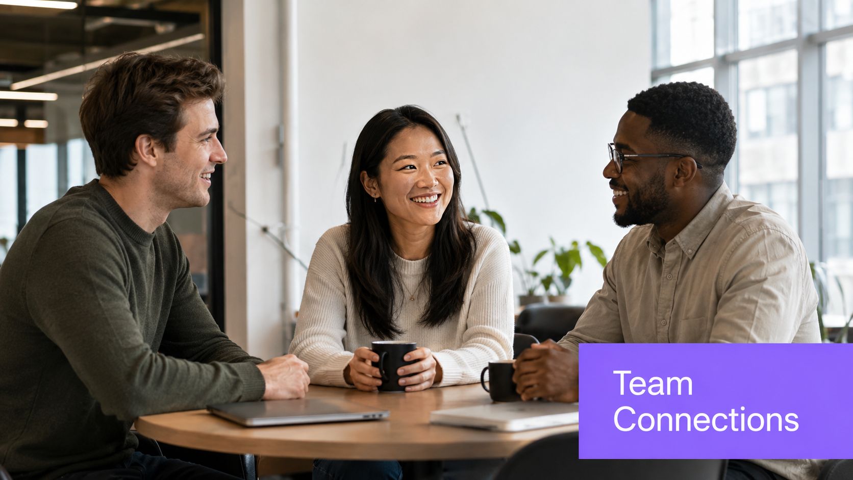 Three diverse professional colleagues smiling and discussing during a friendly team meeting at an office table.